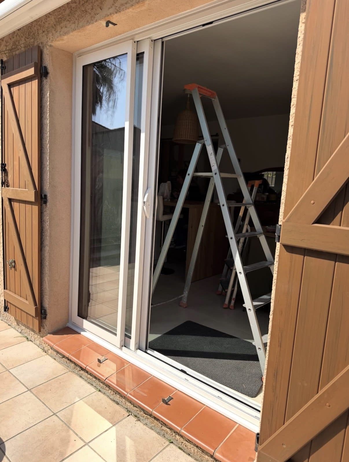 Baie coulissante aluminium blanc installée sur une maison avec volets en bois