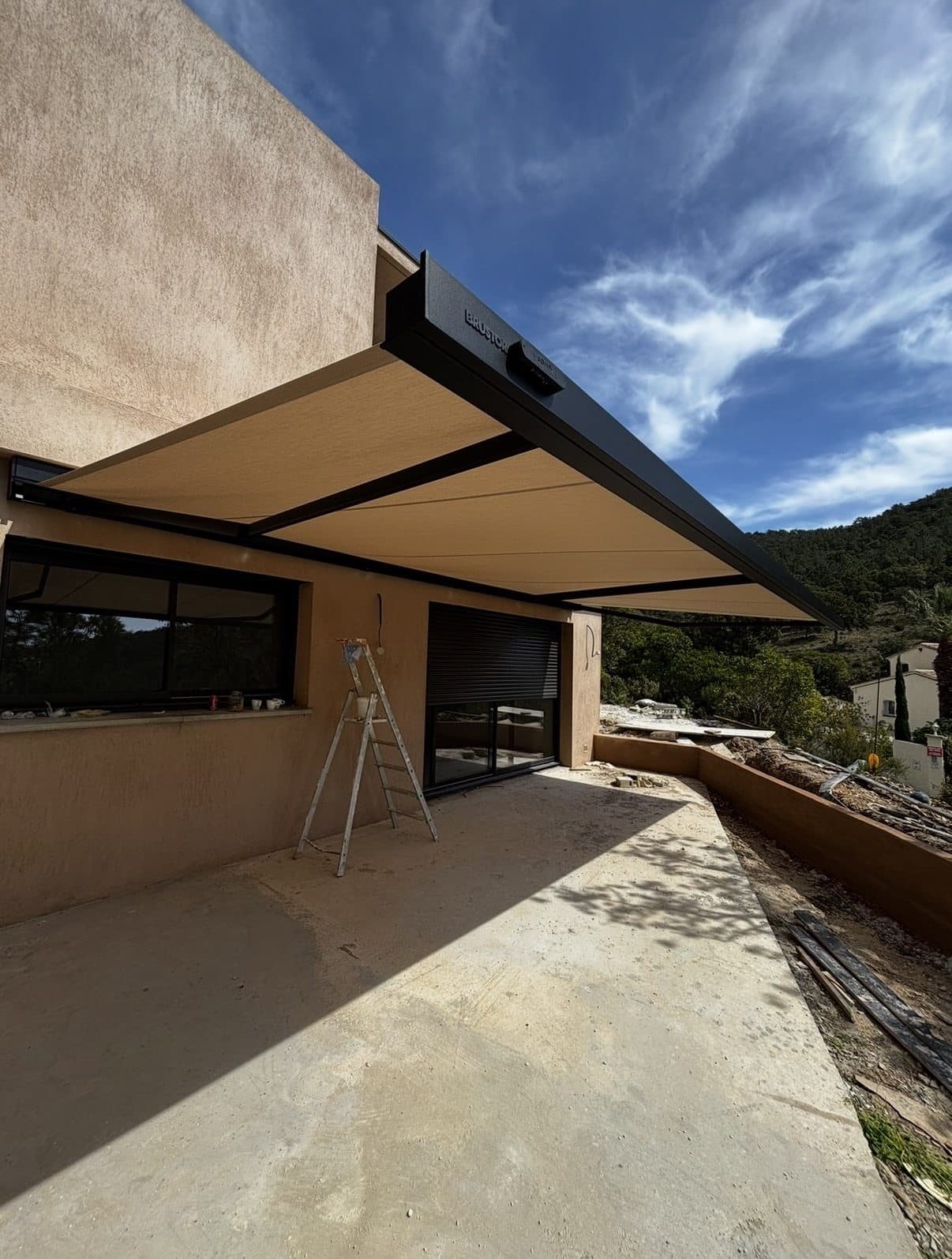Store banne à coffre sombre déployé sur une grande terrasse avec vue sur les collines