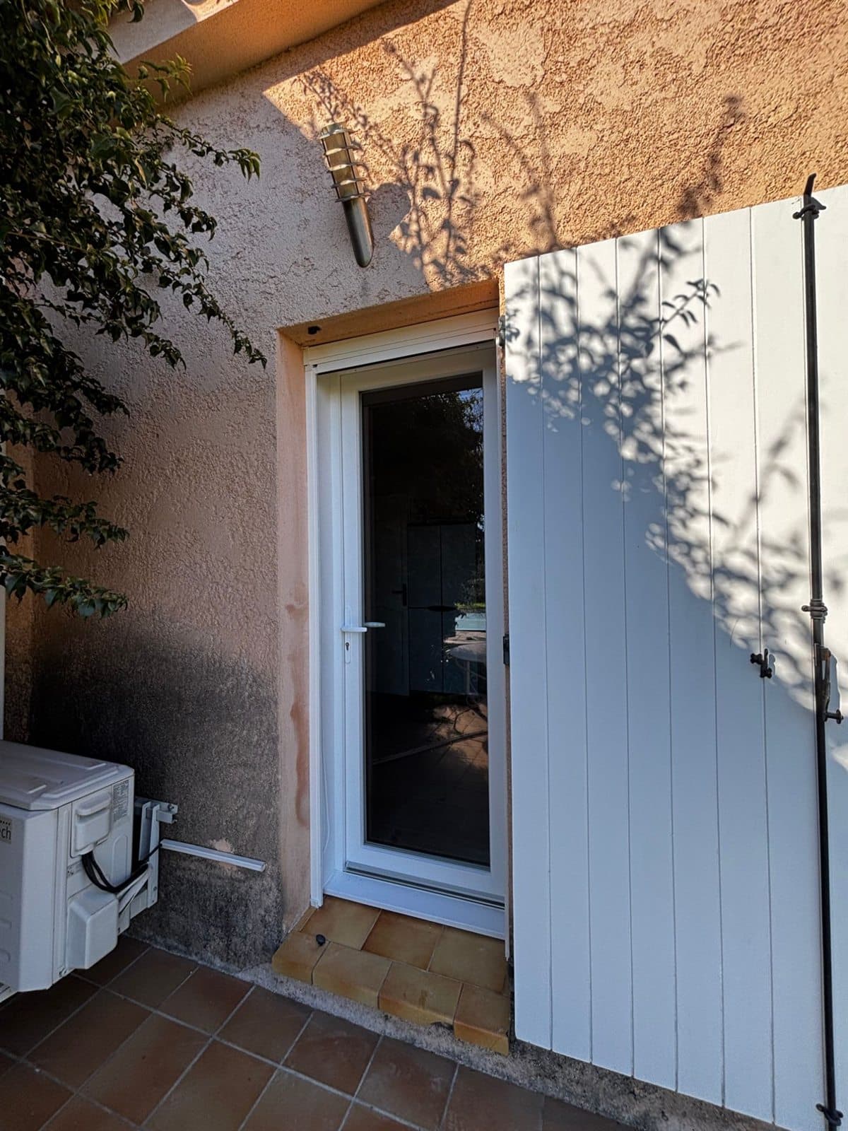 Porte-fenêtre blanche en aluminium posée sur la façade d'une villa provençale, avec volet blanc ouvert